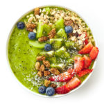 breakfast kiwi smoothie bowl topped with oat flakes and berries isolated on white background, top view